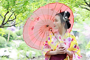 Traditional Asian Japanese beautiful Geisha woman wears kimono bride with a red umbrella in a graden