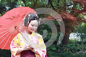 Traditional Asian Japanese beautiful Geisha woman wears kimono hold a umbrella on hand under a tree in a summer graden