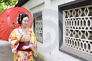 Traditional Asian Japanese beautiful Geisha bride woman wears kimono hold a umbrella in a summer nature garden