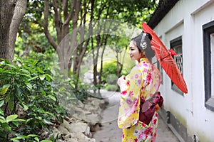 Traditional Asian Japanese beautiful bride Geisha woman wears kimono hold a white red umbrella in a summer nature garden