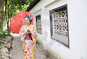 Traditional Asian Japanese beautiful bride Geisha woman wears kimono hold a white red umbrella in a summer nature garden