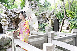 Traditional Asian Japanese beautiful woman bride wears kimono with white umbrella stand by bamboo in outdoor spring garden