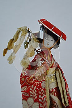 Japanese woman porcelain doll in red coat with decorative red hat and branch of broadleaved tree in hand