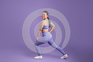 Japanese young woman stretching legs doing lunges on purple studio background