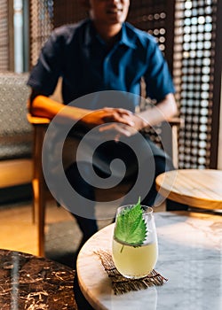 Japanese Yuzu Cocktail with Shiso Leaves Green Perilla in glass on marble low table with blur mixologist in background