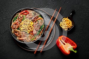 Japchae in black bowl on dark slate table top. Korean cuisine glass chapchae noodles dish with vegetables and meat