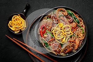 Japchae in black bowl on dark slate table top. Korean cuisine glass chapchae noodles dish with vegetables and meat