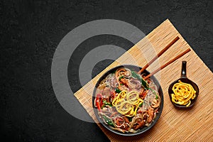 Japchae in black bowl on dark slate table top. Korean cuisine glass chapchae noodles dish with vegetables and meat