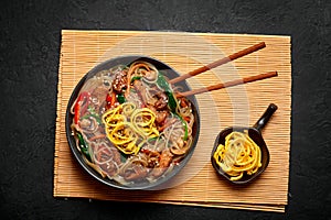 Japchae in black bowl on dark slate table top. Korean cuisine glass chapchae noodles dish with vegetables and meat