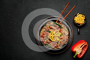 Japchae in black bowl on dark slate table top. Korean cuisine glass chapchae noodles dish with vegetables and meat