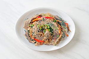 Japchae or stir-fried Korean vermicelli noodles with vegetables and pork topped with white sesame