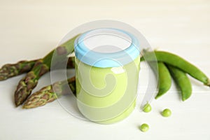 Jar with baby food, fresh pea pods and asparagus on white table