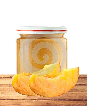 Jar of baby puree and peach slice on wooden table isolated