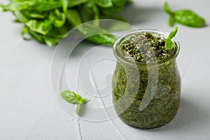 Jar with basil pesto sauce on table.