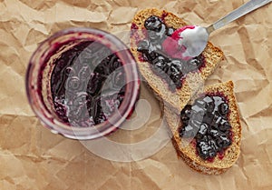Jar of black currant jam with bread for breakfast from above