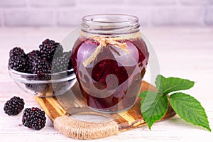 A jar of blackberry jam on a white wooden background.