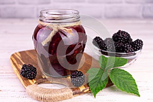 A jar of blackberry jam on a white wooden background.