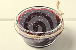 Jar of of blackcurrant jam on white wooden background.