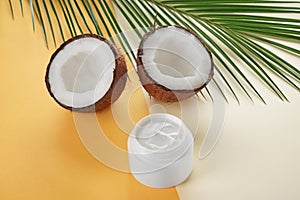 Jar with body cream and coconut on color background