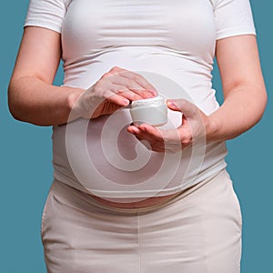 Jar of body cream in pregnant woman, studio shot on blue background