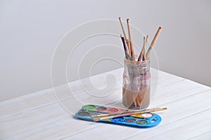 Jar with brushes and watercolors on wooden table