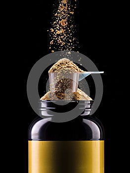 Jar of chocolate protein with scoop and falling powder isolated on black