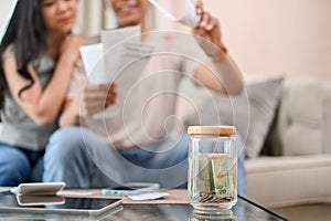 A jar of coins on a coffee table with a stressed couple planning their finances