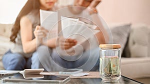 A jar of coins on a coffee table with a stressed couple planning their finances