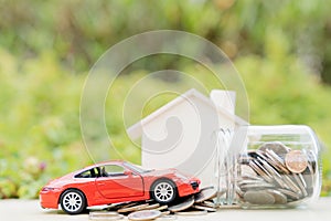 Jar of coins and red car on pile of coin on blurred green natural background. Saving money and investment concept