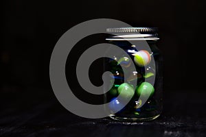 Jar with colored marbles on a black surface photo