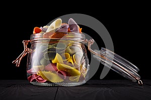 Jar of colorful farfalle pasta on wooden table  on black background