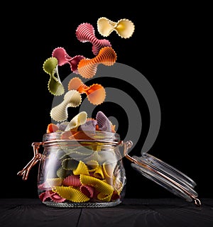 Jar of colorful farfalle pasta on wooden table  on black background