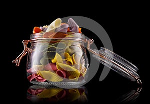 Jar of colorful farfalle pasta on wooden table  on black background