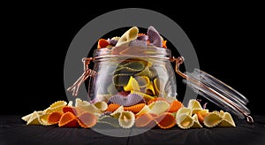 Jar of colorful farfalle pasta on wooden table isolated on black background