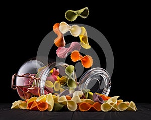 Jar of colorful farfalle pasta on wooden table isolated on black background