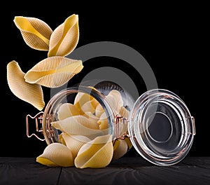 Jar of conchiglie pasta shell on wooden table  on black background