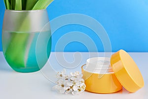 Jar of cosmetic cream and soft green vase with flowers on pink background. Natural cosmetic product with herbs