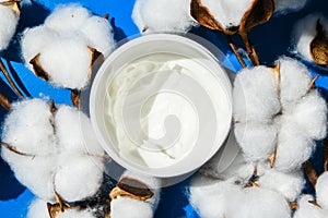 Jar of cream on a blue background. Mockup for label. Natural cosmetics. Cotton flowers, Moisturizer cream next to cotton flowers,