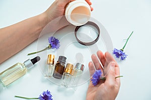 Jar of cream in caucasian woman's hand, blue flowers, glass cosmetical bottles closeup and blurred hand with flower. Natural