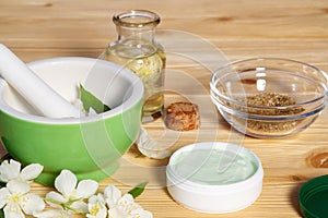 Jar of cream made from natural plant ingredients, oils and herbs, jasmine flowers, mortar and pestle on a light wooden