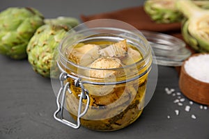 Jar of delicious artichokes pickled in olive oil on grey table, closeup