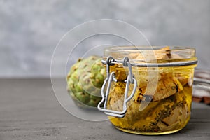 Jar of delicious artichokes pickled in olive oil on grey wooden table, closeup. Space for text