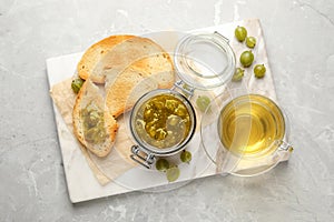 Jar of delicious gooseberry jam, bread, fresh berries and tea on grey marble table, top view