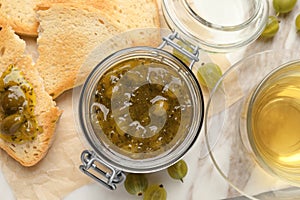 Jar of delicious gooseberry jam, tea and bread on table, flat lay