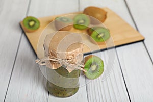 Jar of delicious kiwi jam and fresh fruits on white wooden table