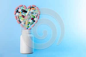 Jar of different tablets and pills in shape of heart on top of it. Multi-colored pills in the shape of heart on. Concept
