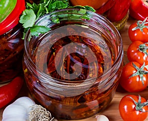 Jar of dried tomatoes in olive oil among fresh vegetables