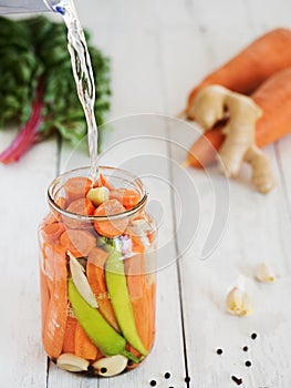 Jar with fermented peppers carrots, garlic and ginger. Pouring pickle vegetables. Harvesting. Canned vegetarian food, concept.