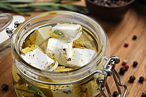 Jar with feta cheese marinated in oil on wooden table. Pickled food
