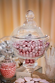 Jar Filled with Pink Foil Wrapped Chocolate Candy, Jelly Beans and Heart Shaped Cookies On A Table Decorated for a Wedding